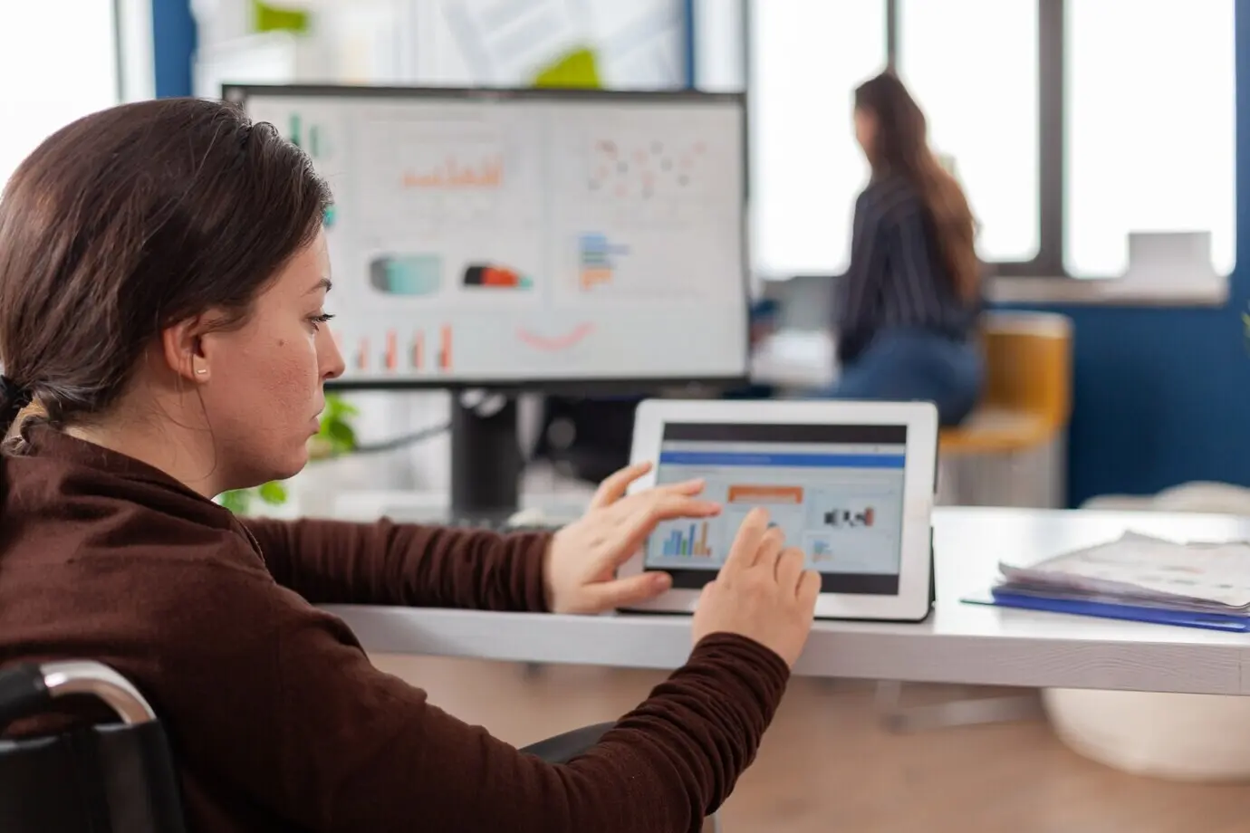 Женщина-предприниматель использует компьютер и планшет, проверяя статистические данные в офисе бизнес-стартапа.